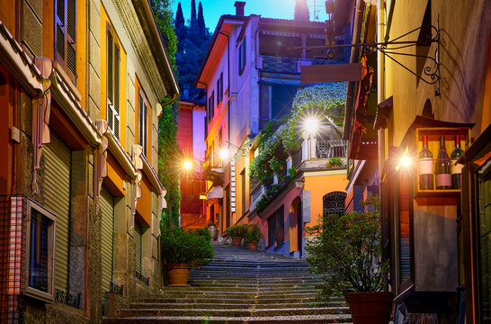Bellagio village at lake Como near Milan Italy, region Lombardy. Night view of famous street with paving stones stairs and cosy restaurants during sunrise with glowing lanterns and old houses walls.