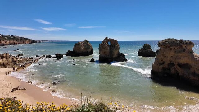 Powerful Atlantic waves roll onto the sandy shore beside rugged rock formations at Praia dos Arrifes, a beautifully wild and unspoiled stretch of coastline along the Algarve, famous place