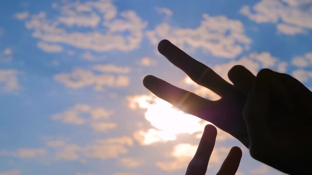 Silhouettes of four hands are showing victory sign, gesture of peace against the sunset or sunrise sky - close up, sun lens flare. Unity, harmony, friendship and positive concept