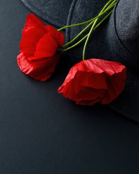 anzac day poppy flowers and military hat on dark background