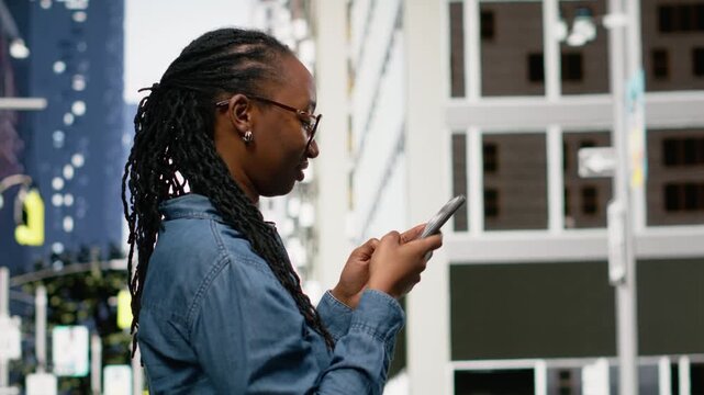 Using navigation app on smartphone, black woman walking around the city. Girl strolling and exploring metropolitan downtown area with tall buildings on city streets, following map route.