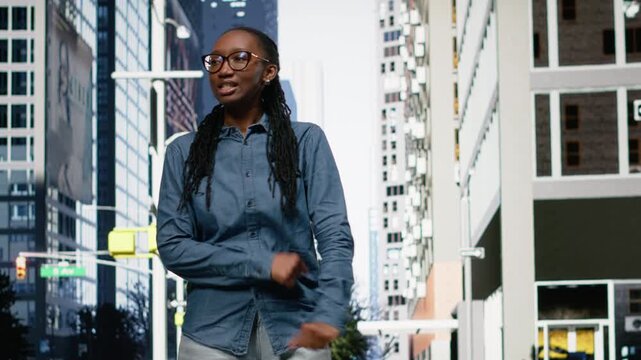Excited black woman dancing on city street after receiving good news, positive emotion on sidewalk. Overjoyed young adult outside celebrating with fun dynamic dance moves, urban fashion.