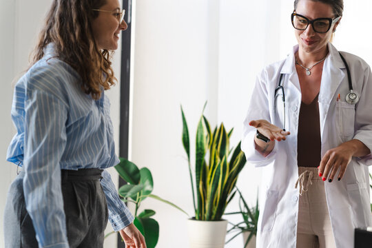 A doctor in a white coat speaks with a patient, gesturing with her hand during a consultation in a bright, modern office.