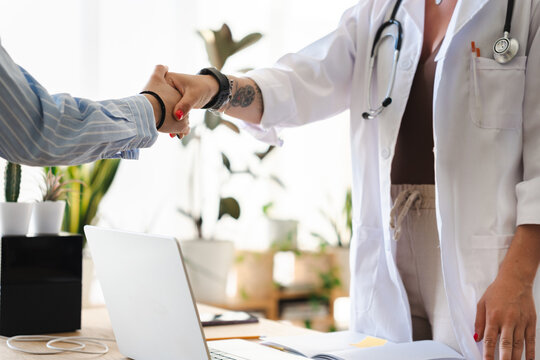A doctor in a white coat shakes hands with a patient, symbolizing trust and a successful consultation in a modern medical office.