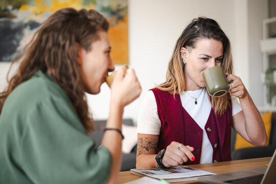 Two women enjoy coffee while discussing documents at a table, with a laptop nearby.