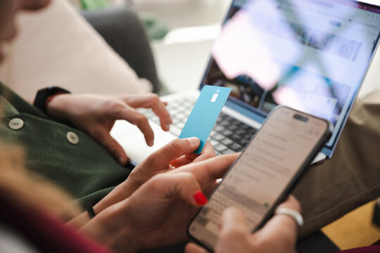 A person uses a credit card and a smartphone to make an online purchase on a laptop.