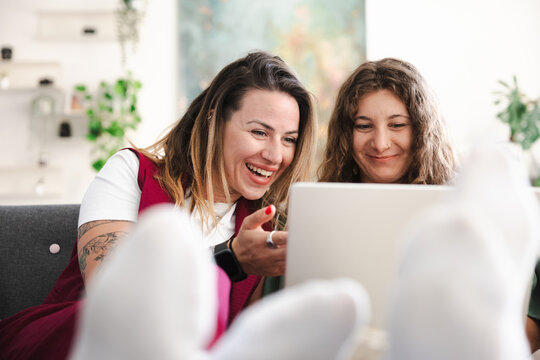 Two women are laughing while looking at a laptop screen together, enjoying a shared moment of amusement and connection.