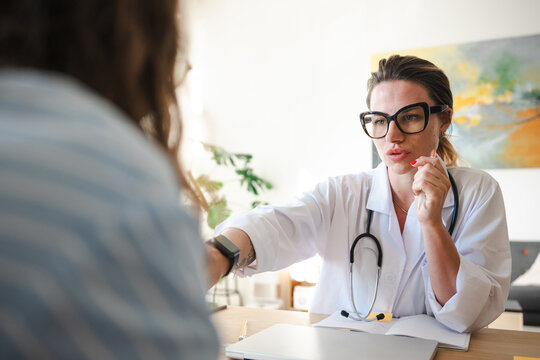 A doctor in a white coat consults with a patient, discussing medical information during an appointment in a bright office setting.