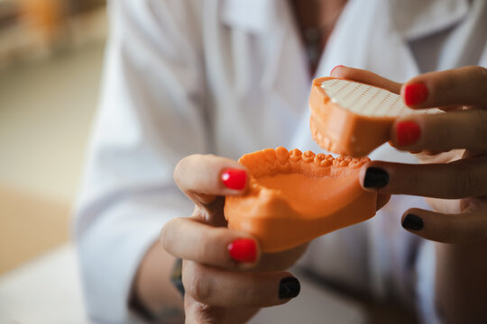 A person in a white coat holds an orange dental mold with teeth, demonstrating a dental procedure or model.