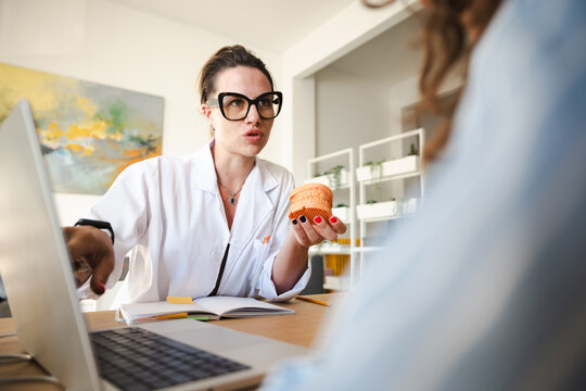A dentist in a white coat explains a dental model to a patient during a consultation in a modern office.