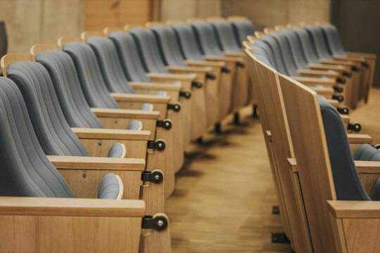 Rows of modern wooden auditorium chairs with blue upholstery arranged in a neat formation, showcasing a contemporary interior design in a spacious hall