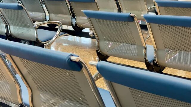 Empty metal benches at railway station, rows of blue cushioned perforated seats with chrome frames reflecting light on polished