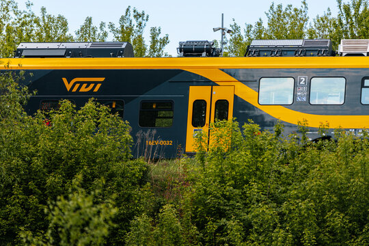 Riga, Latvia - May 15, 2026: Modern train with yellow and gray design partially obscured by greenery, showcasing the VVT logo and solar panels on the roof