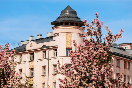 Historic building with ornate architecture and a conical roof surrounded by blooming cherry blossom trees under a clear blue sky in a vibrant urban setting