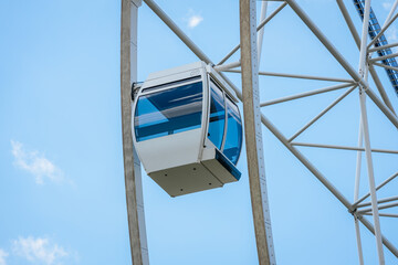 White gondola of a Ferris wheel suspended against a clear blue sky, showcasing the structure's metal framework and modern design elements © Emvats