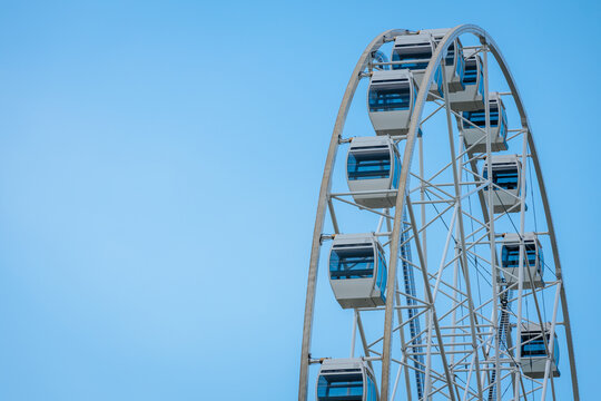 Large Ferris wheel with white cabins against a clear blue sky, showcasing a modern amusement park attraction in a vibrant outdoor setting