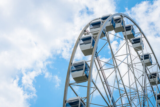 Ferris wheel structure with blue and white cabins against a bright sky with fluffy clouds, showcasing a popular amusement park attraction in a recreational area
