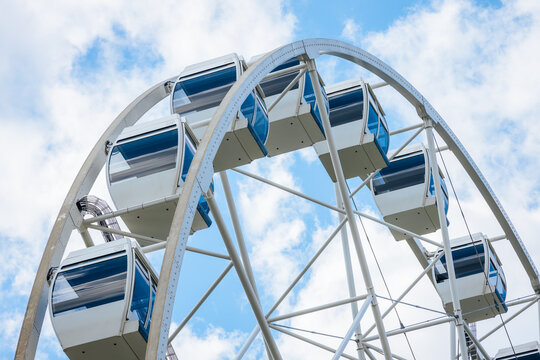 White and blue ferris wheel with enclosed cabins against a bright sky, showcasing a modern amusement park attraction in a recreational setting
