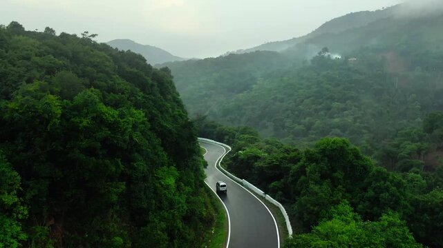 Birds-eye view of a white vehicle navigating sharp hairpin turns on a lush green mountain road, cinematic road trip concept
