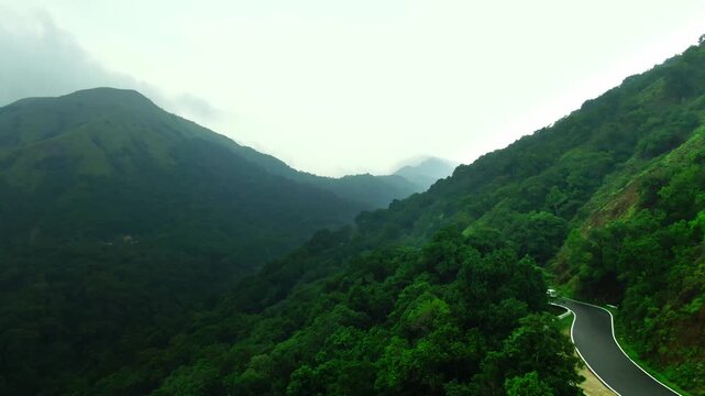 Birds-eye view of a white vehicle navigating sharp hairpin turns on a lush green mountain road, cinematic road trip concept.