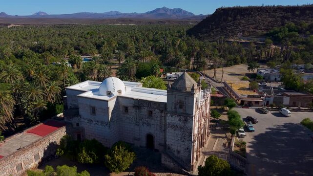 Aerial views show Mission Church in San Ignacio, Baja California. The church sits in an oasis surrounded by palm trees and mountains. High quality 4k footage