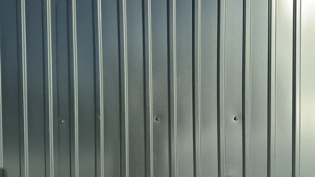 Corrugated metal fence panels shimmering in sunlight, closeup of galvanized steel ridges with subtle dents and visible screws.