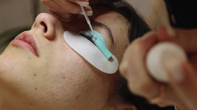 The hands of a cosmetologist laminates the eyelashes of a teenager, applying the product.