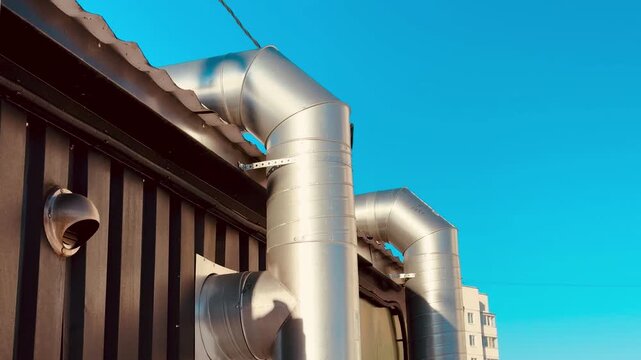 Restaurant exterior ventilation pipes gleaming brightly, stainless ductwork mounted on corrugated facade, sky blue background.