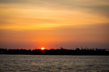 Fototapeta premium Beautiful sunset over calm water with orange sky and silhouette landscape during evening twilight.