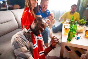 Fototapeta premium Friends gather in a living room to watch a sports event. They wear team shirts and show excitement. Drinks and snacks are on the table while smiles are shared among the group.