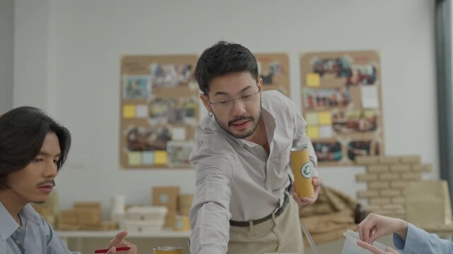 Adult asian man with glasses standing office presentation, speaking about sustainable packaging design, holding recycled paper tube, discussing team workshop collaboration and business startup