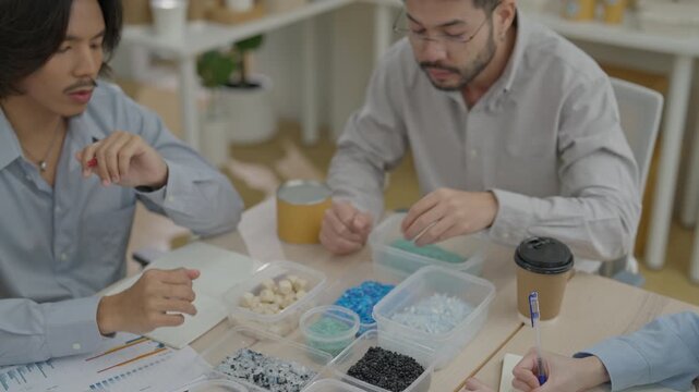 Adult men discuss plastic pellet sample material at office meeting table, business team reviewing plastic granule sample container, creative workplace discussion collaboration product design￼