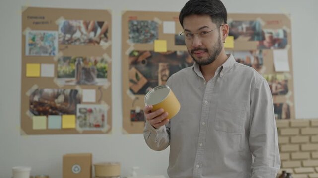 Man holding yellow can office with notice board, portrait, smiling, product mockup, young man examining paper container office with package prototypes and concept board, man inspecting yellow paint