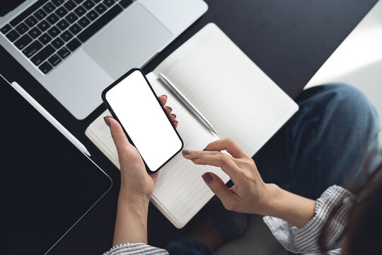 Smartphone white screen mockup, Business woman using smartphone with empty screen with laptop and notebook on table at home office, top view