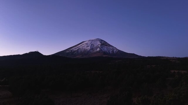 Majestic Silhouette of Snow-Capped Popocatepetl Volcano, a pine forest and a fumarole at Blue Hour, 4K 60fs horizontal forwards aerial drone shot before sunrise