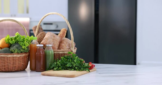 Fresh vegetables, fruits, bread and drinks on white marble kitchen island indoors, camera moving right