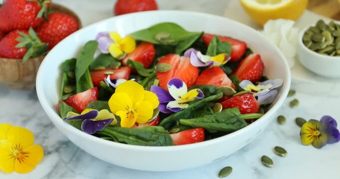 Woman adding pansy flower to delicious salad at table, closeup