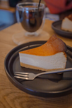 Slice of Basque burnt cheesecake and iced coffee on a wooden cafe table