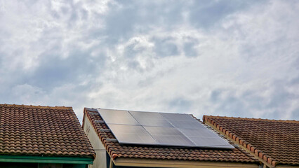 Fototapeta premium Solar Panels on a Tiled Residential Roof Under a Cloudy Sky