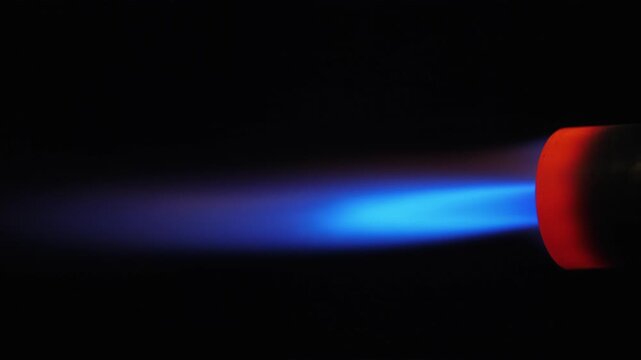 Close up of blue flame jetting from gas torch nozzle in darkness, abstract fiery motion.