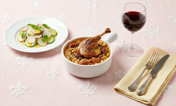 Traditional French cassoulet with confit duck leg served with a glass of red wine and radish salad.

