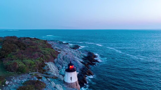 Castle Hill Lighthouse aerial hyperlapse, a fast drone push-in shot flying directly over the historic beacon on a rocky cliffside point at twilight in Newport, Rhode Island.