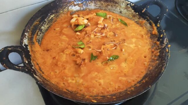 Indonesian spicy squid dish simmering in a red chili sauce, topped with fresh basil and lime leaves in a wok