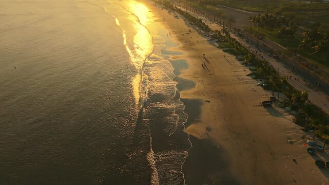Vietnam, Da Nang Golden Sunset Along Da Nang Shoreline, Aerial Sweep Of Lively Beach With Shimmering Water Trail, Waves Meeting Sand, Beach Umbrellas And Small Boats, Local Asian Vendors