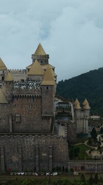Vertical screen, Vietnam, Da Nang, Ba Na Hills Imposing Stone Wall With Battlements And Ramparts, Rugged Faade, Mountain Backdrop, Narrow Service Paths, Weathered Stonework, Moody Overcast
