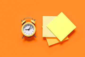 Fototapeta premium Alarm clock with sticky notes on orange background. Time management concept