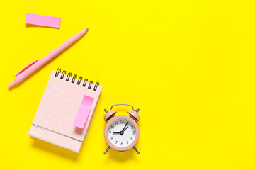 Fototapeta premium Alarm clock with calendar and sticky note on yellow background. Time management concept