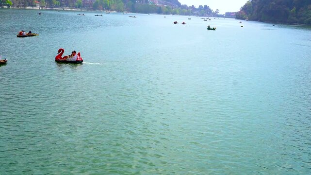 Panoramic wide-angle view of a red swan pedal boat and rowing boats on Naini Lake, Nainital