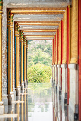 Obraz premium Long perspective corridor inside a Thai temple featuring golden frames, colorful columns, and symmetrical Buddhist architectural details.