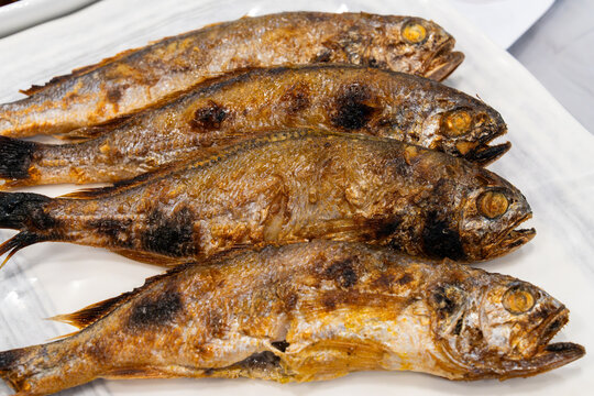 Overhead view of four whole grilled dried yellow croaker fish on a white platter
